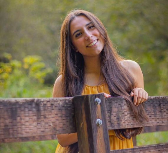 Melina leans against a wall wearing a green shirt